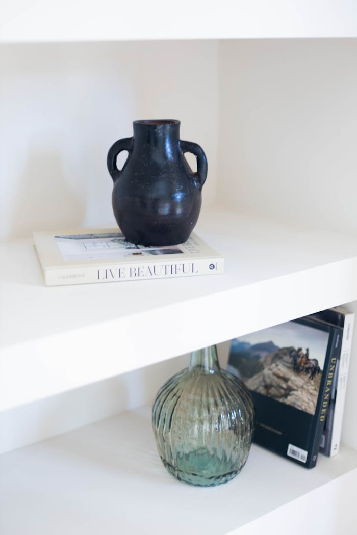 A minimalist shelf featuring a ceramic vase and books, exuding elegance and simplicity.