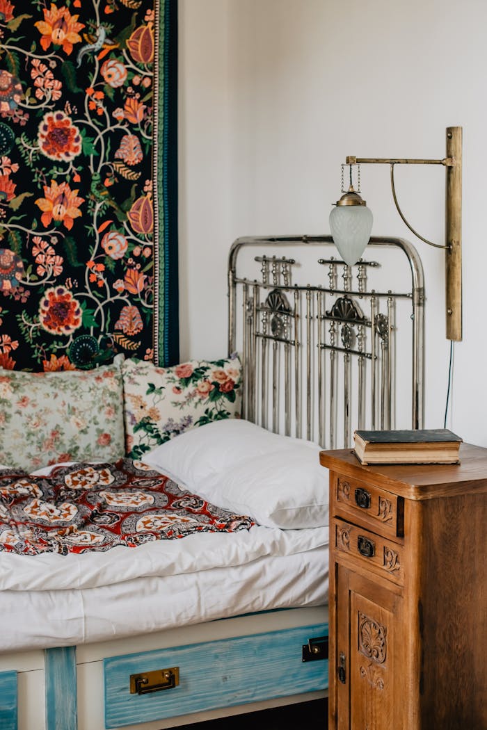 Cozy vintage bedroom featuring floral decor, antique iron bedframe, and wooden nightstand.
